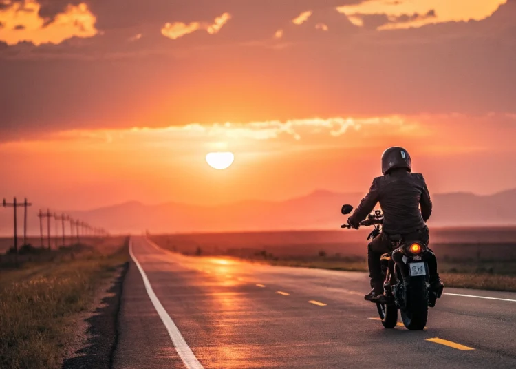 A motorcyclist riding towards the sunset on a long open road