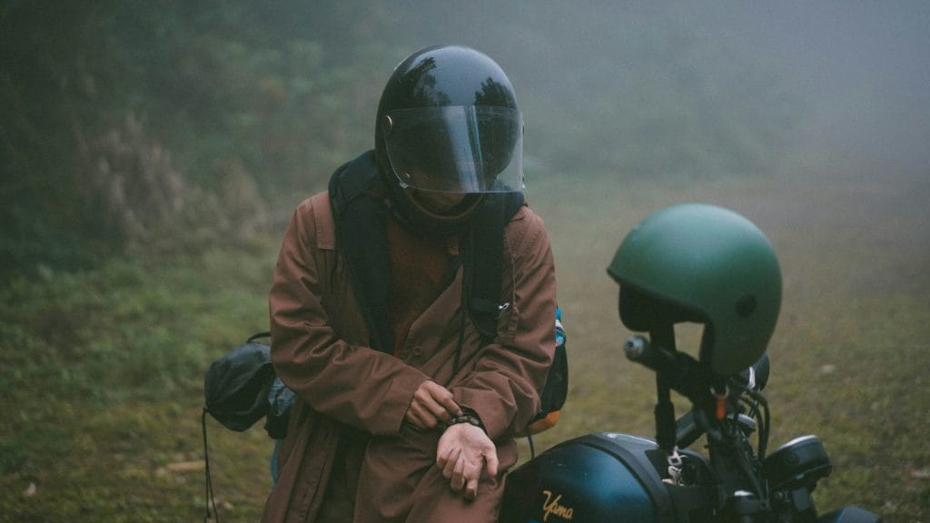 A rider pausing beside their motorcycle on a misty morning